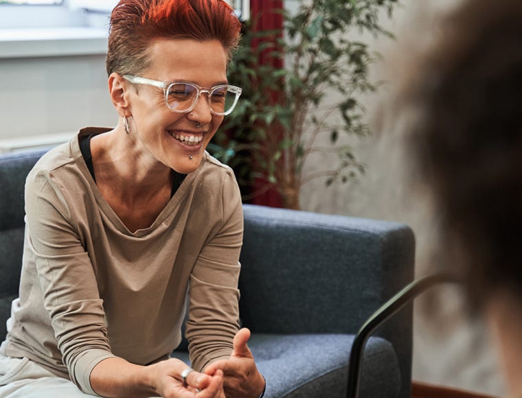 Healing therapy. Happy red haired woman laughing out loud while sitting at the sofa and talking with her doctor during therapy. Mental health concept