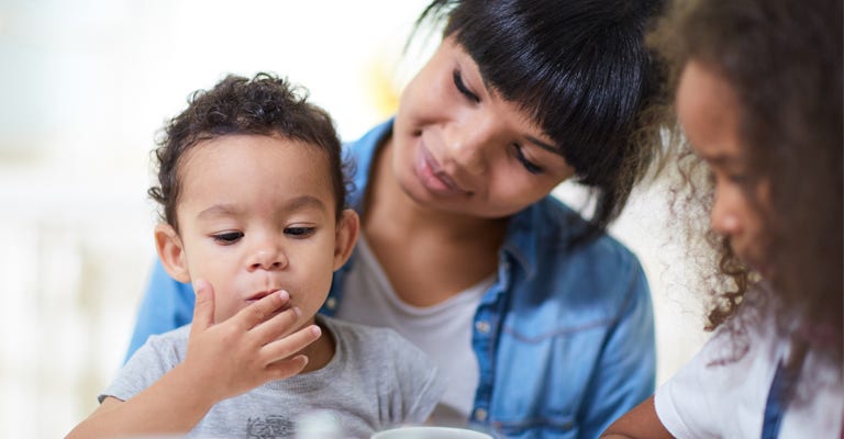 Hungry toddler eating something with mother and sister near by